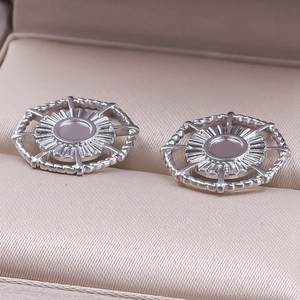 Detailed view of silver stainless steel round stud earrings with sunburst pattern on beige cushion
