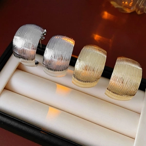 Close-up of gold and silver C-shaped striped earrings on a soft jewelry display cushion