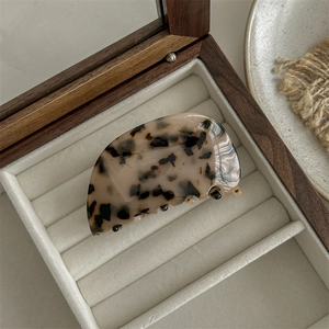Macro view of light tortoiseshell leopard acetate hair claw clip on a beige jewelry box
