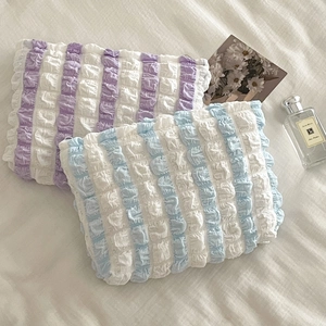 Macro detail of pleated puff sleeve cosmetic bags with striped texture on white linen