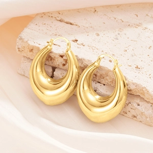 Close-up of chunky gold-plated teardrop hoop earrings resting on a textured stone