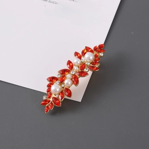 Detail of a golden hair clip featuring red leaf-shaped rhinestones and white pearls