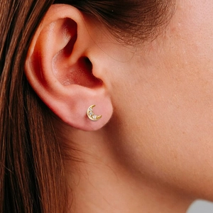 Close-up of a gold moon-shaped earring with zircon stones worn on the earlobe