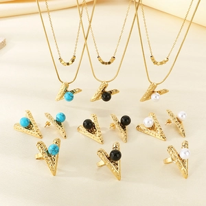 Gold stainless steel jewelry set featuring V-shaped pendants and pearls on beige fabric