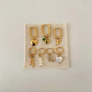 Detailed set of seven golden hoop earrings with heart, pearl, and letter charms on linen