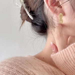Close-up of gold irregular oval earrings with hammered texture on female model