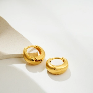Macro detail of thick 18K gold plated hoop earrings with a polished glossy metallic finish