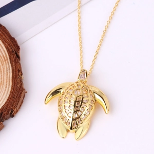 Golden sea turtle pendant necklace with clear baguette crystals on a white surface