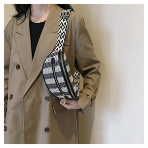 Detail of checkered crescent crossbody bag with woven strap on a trench coat