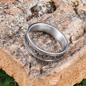 Silver stainless steel ring with wave pattern on rustic bark in outdoor nature