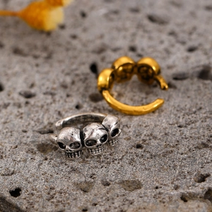 Macro shot of skull claw ear cuffs in antique silver and gold finishes on a stone surface