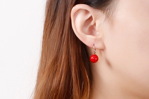 Vue détaillée d'une femme portant des boucles d'oreilles perles rouges et crochets or rose