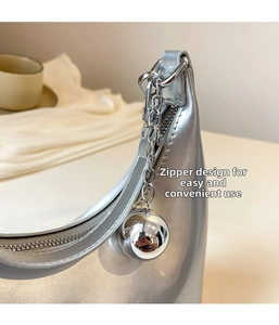 Detail of silver metallic hobo bag featuring a smooth zipper and a large sphere charm