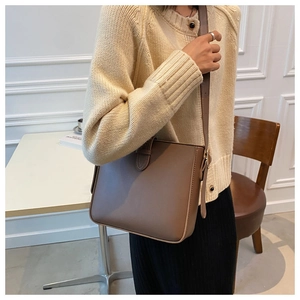 Brown faux leather crossbody bucket bag shown on model in a warm indoor setting
