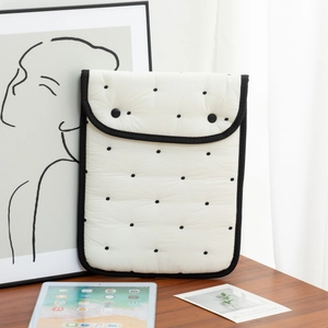 Close-up of quilted cream polka dot laptop sleeve with black trim and button closure