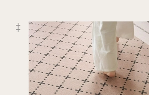 Close-up of soft pink vintage carpet with black cross pattern and bare feet on it