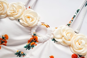 Détail d'un maillot blanc avec imprimé floral orange et décorations de roses en tissu