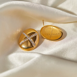 Detail of 18k gold teardrop earrings with crystals and cross motif on silk fabric
