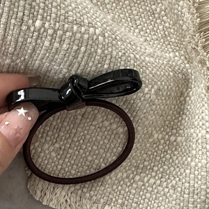 Close-up of a black satin bow hair tie with a brown elastic band on beige fabric