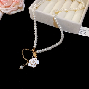 Detailed macro view of white enamel camellia pendant with gold trim on pearl necklace