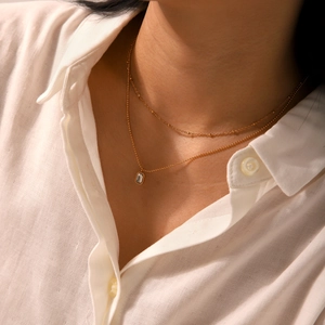 Detail of double-layer gold chain necklace with a rectangular zircon pendant on model