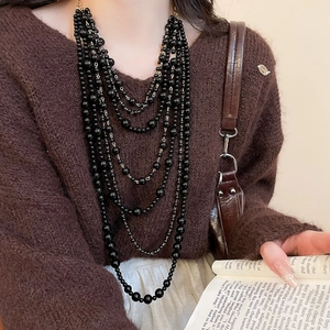 Detail of multi-layered black acrylic beaded necklace on brown knitted sweater