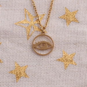 Collier doré en titane avec pendentif œil maléfique sur tissu blanc à motifs étoiles