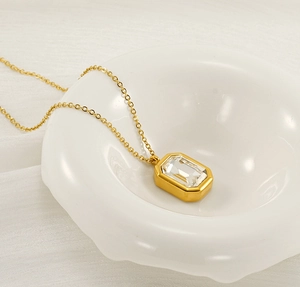 Macro shot of a gold chain necklace with a rectangular clear crystal pendant on white decor