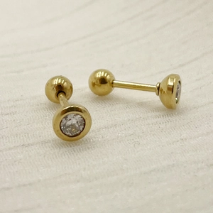 Macro detail of gold titanium steel stud earrings featuring clear cubic zirconia and ball backs