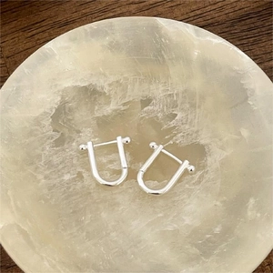 Detailed view of silver U-shaped horseshoe earrings with spherical ends in a stone tray