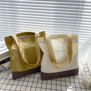 Detail of two-tone canvas tote bags in mustard green and beige with large front pocket