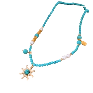 Ethnic turquoise beaded necklace with sun pendant and gold fortune charm on white background