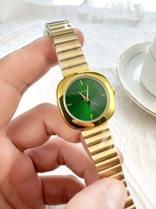 Detail of elegant gold women's watch with green dial and metallic stretch band in life scene