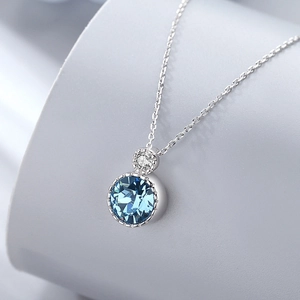 Detailed close-up of a silver necklace featuring a round blue crystal pendant with bead edge