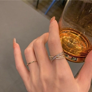 Détail de la bague multicouche dorée avec zircons portée par une femme tenant un verre