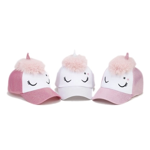 Close-up of glitter unicorn baseball caps with faux fur pom-poms and sequin details
