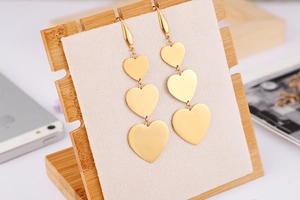Macro view of gold-plated triple heart drop earrings showing polished tiered finish
