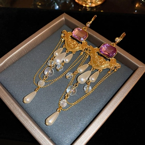 Détail de boucles d'oreilles vintage avec gemmes mauves et perles dans un écrin