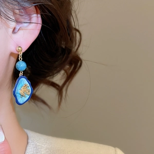 Vue détaillée de boucles d'oreilles ovales avec émail bleu et incrustation corail doré