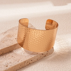 Close-up of golden wide open cuff bracelet with hammered texture on natural stone