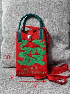 Detail view of red knitted phone bag with green Fa character and Good Luck text slogan