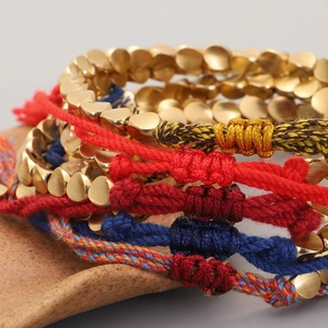 Detalle macro de pulsera tejida a mano con cuentas de corazón doradas y adorno de borla
