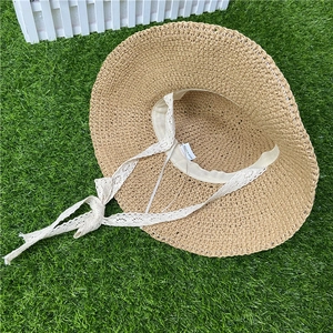 Detailed texture of beige straw sun hat with white lace ribbon on green grass