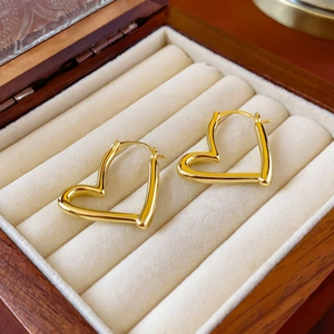 Détail de boucles d'oreilles cœur évidé dorées dans une boîte à bijoux en bois