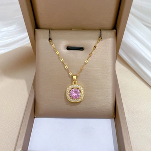 Detail shot of a gold necklace with a pink square pendant in a beige jewelry box