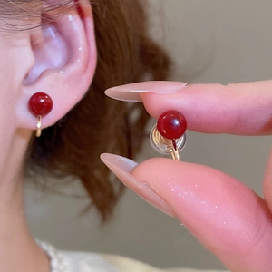 Detail of red bead clip-on earrings with gold finish, shown on model and held by hand