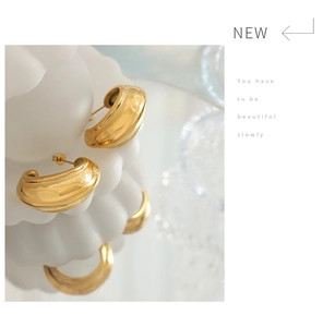 Close-up of chunky gold C-shaped earrings on a wave stand with soft mirror reflections