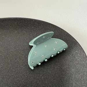 Macro detail of bean green hair claw clip with shimmering rhinestones and matte finish