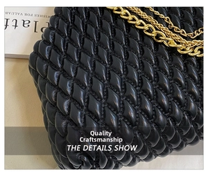 Detail of black quilted shoulder bag featuring woven texture and chunky gold chain strap