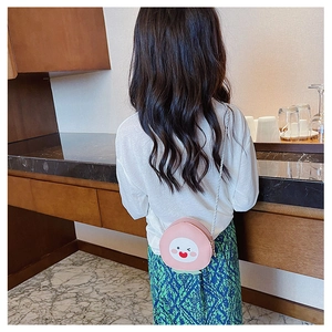 Close-up of pink peach-shaped child's crossbody bag with braided strap and cartoon face